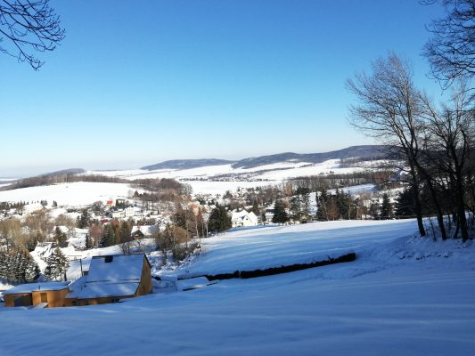 Verschneite Landschaft mit Blick über Steina, Häuser und Hügel unter blauem Himmel im Winter